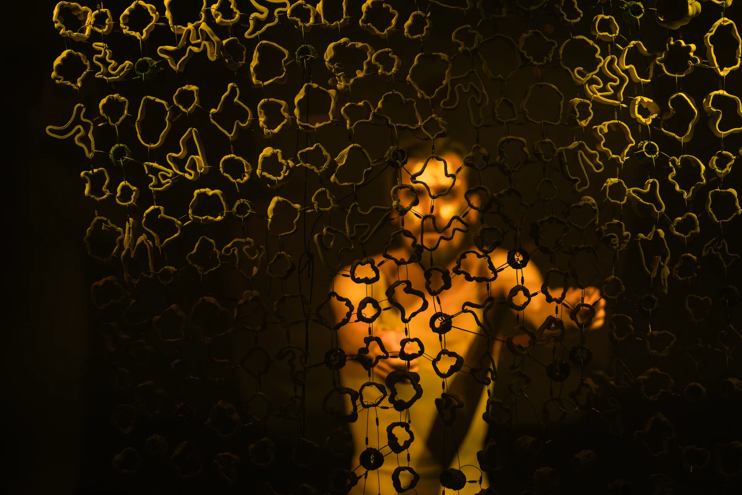 Suspended ceramic forms frame the silhouette of a performer.