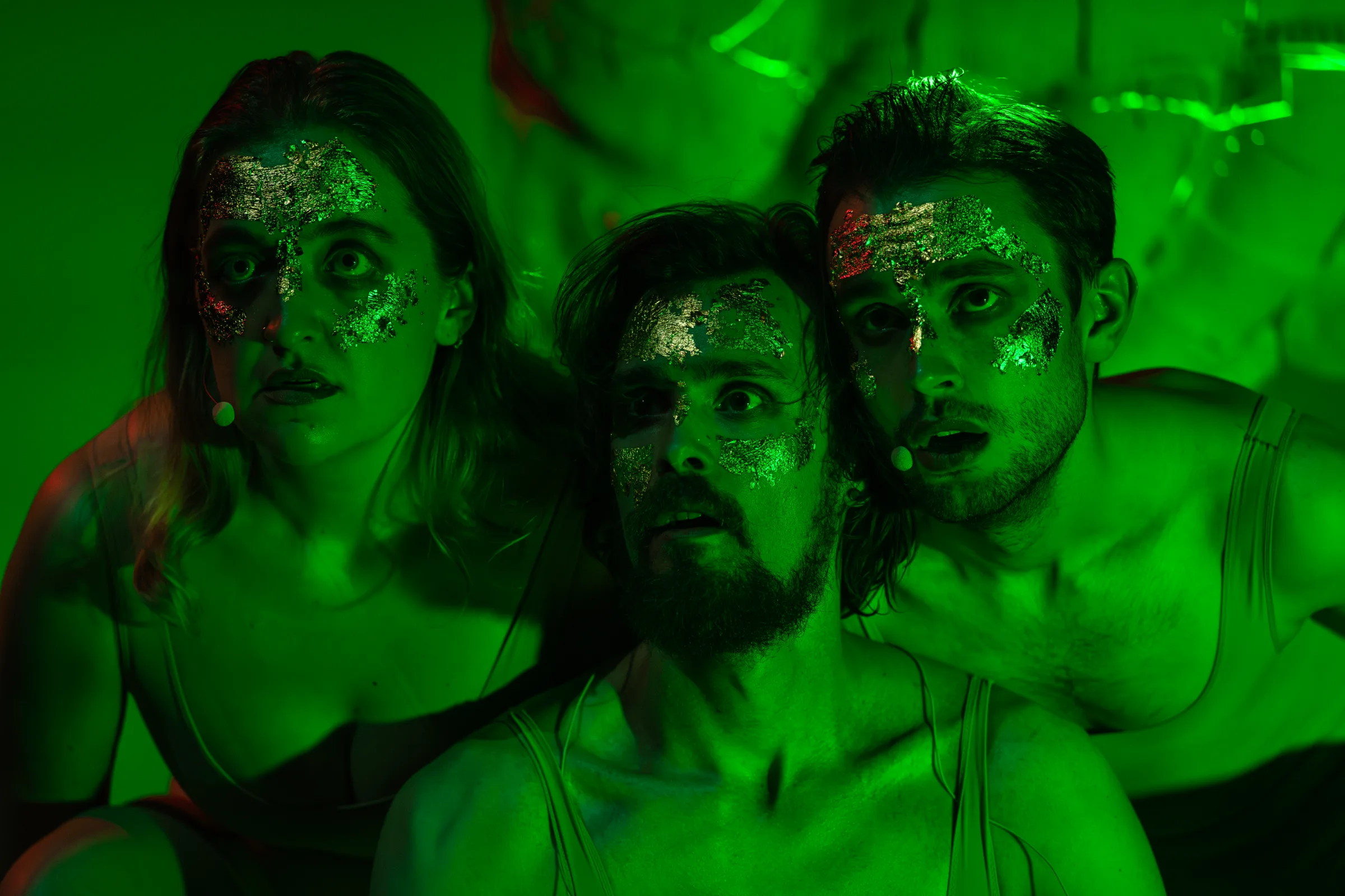 Three performers gather under intense green stage lighting.